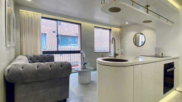 A modern living room with a grey sofa, a round kitchen island with a sink, and large windows with curtains. - Palace by Wynwood House  (Bogotá)