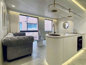 Een moderne woonkamer met een grijze bank, een rond keuken eiland met een spoelbak en grote ramen met gordijnen.