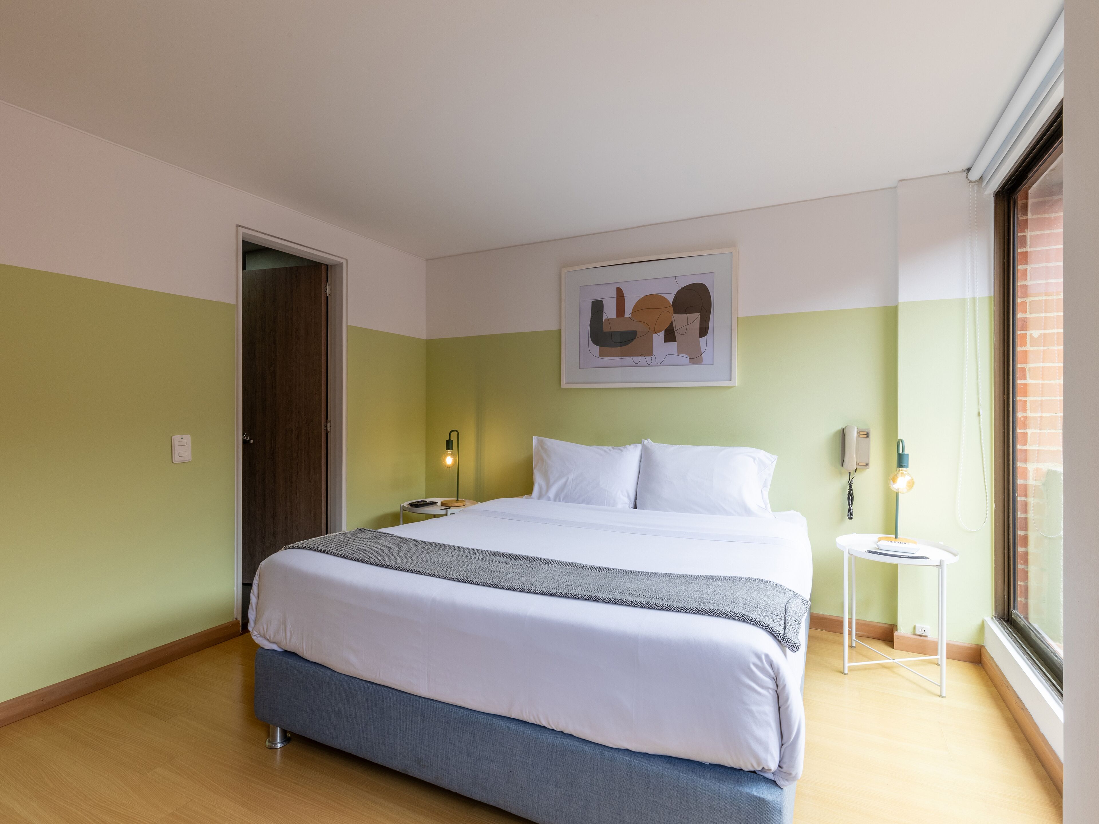 Une chambre d’hôtel avec un lit, une table de chevet, une lampe et une fenêtre donnant sur un paysage.