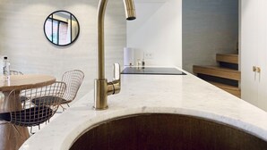 A modern kitchen with a stainless steel sink, a round mirror, and a dining area with a wire chair. - Palace by Wynwood House  (Bogotá)