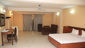 A hotel room with a bed, a desk, two chairs, a ceiling fan, and a window with curtains. - Atlanticoast Residence (Bakau)