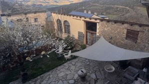 Een terras van natuursteen met buitenmeubilair, een witte zonneluifel en uitzicht op bergen.