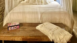 Ein Bett mit Baldachin, ein Holztisch mit einer Schachtel Pralinen und eine weiße Tagesdecke.
