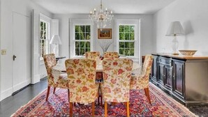 A dining room with a chandelier, floral chairs, a patterned rug, and a cabinet. - Colonial yellowhouse (Newtown)