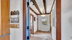 A hallway with a stone floor, wooden beams, and a door with a sign reading "HOME". - Colonial yellowhouse (Newtown)