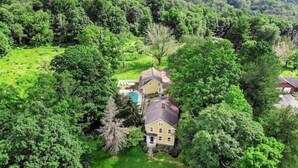 A two-story house surrounded by dense greenery, with a visible swimming pool and a well-maintained lawn. - Colonial yellowhouse (Newtown)