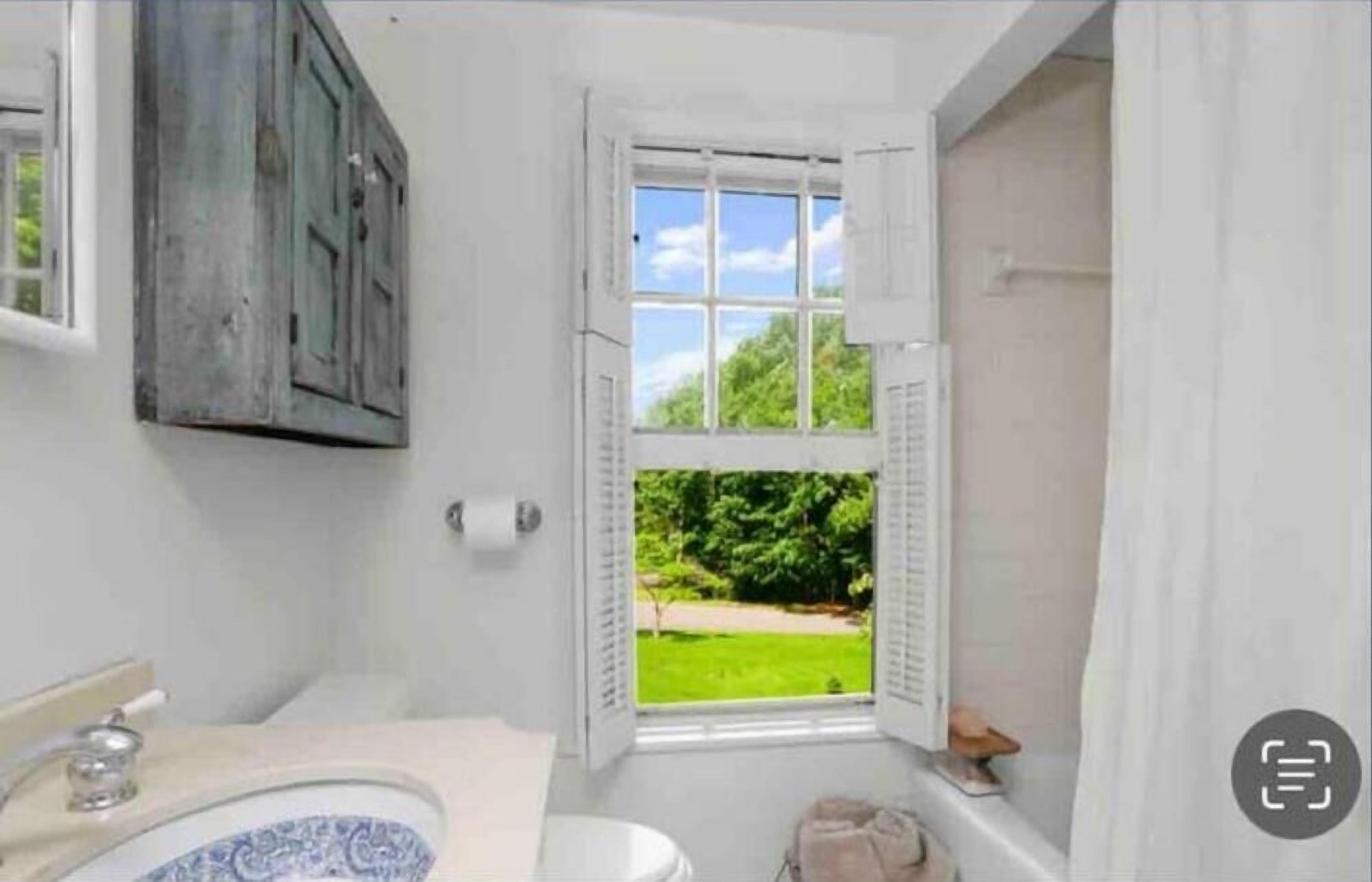 A bathroom with a toilet, sink, and a window with shutters.