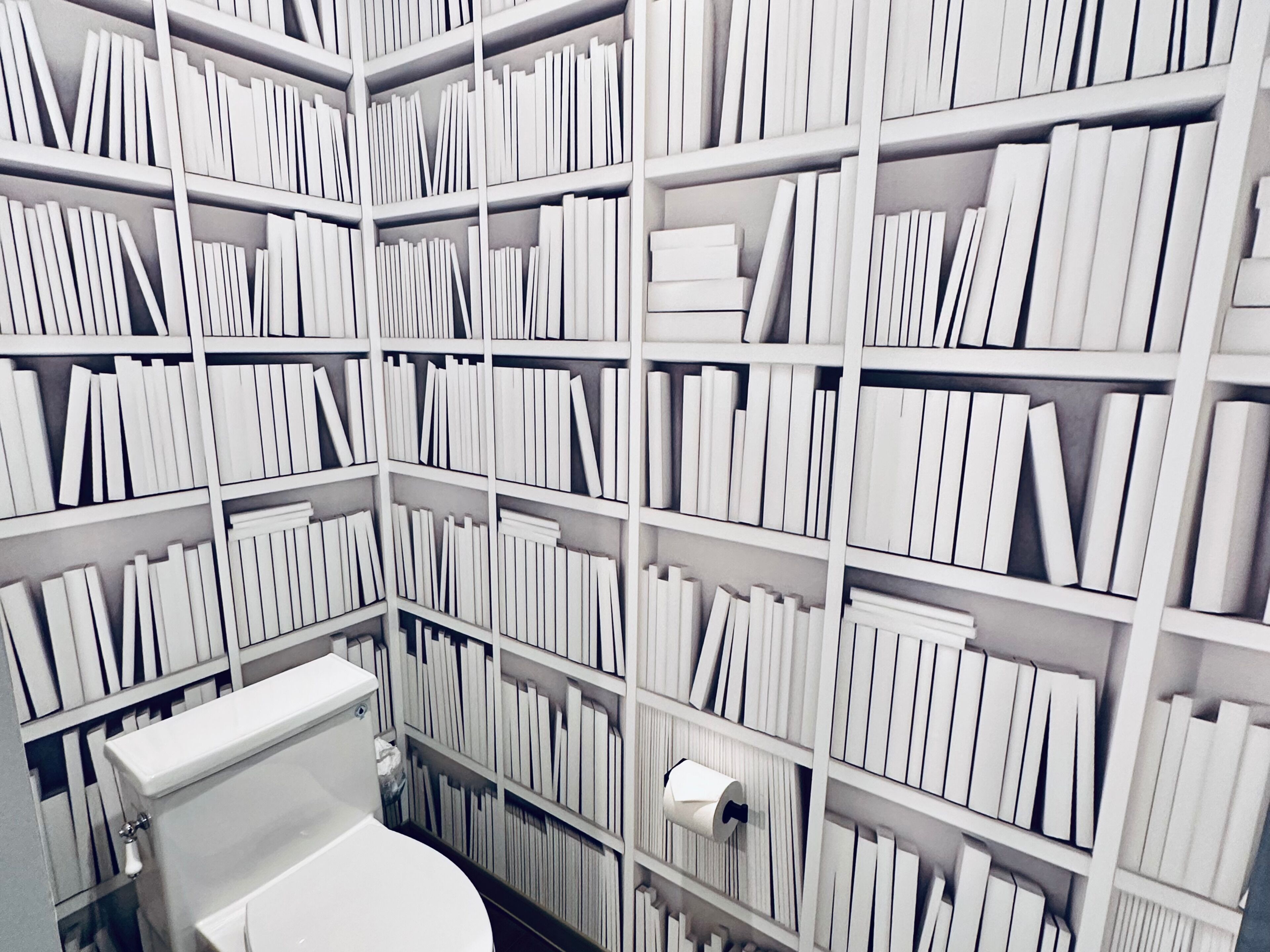 A library with white bookshelves and a white toilet.