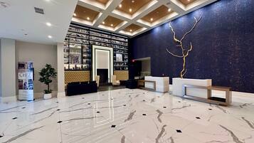 Um hall de hotel com piso de mármore, balcão de recepção, lareira e uma parede com detalhes em folha de ouro.