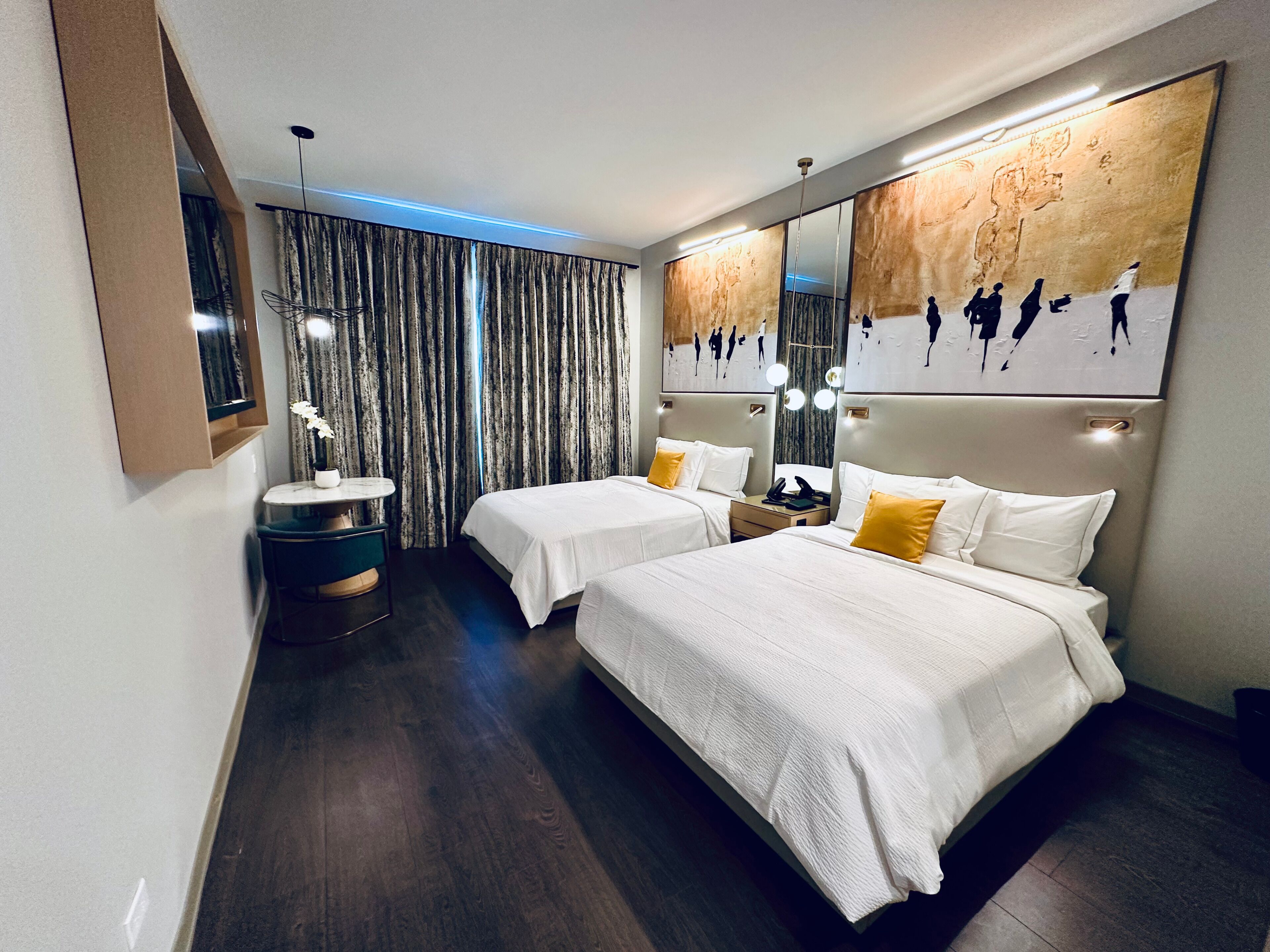 Habitación de hotel con dos camas, una mesa redonda, un espejo y una obra de arte grande en la pared.