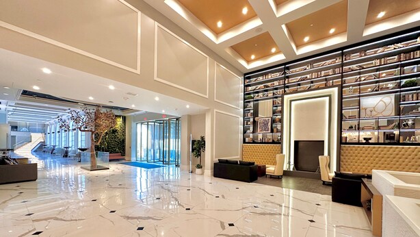 A spacious lobby with a marble floor, a central seating area, and a wall of bookshelves. - Chez Hotel Arlington Heights (Arlington Heights)