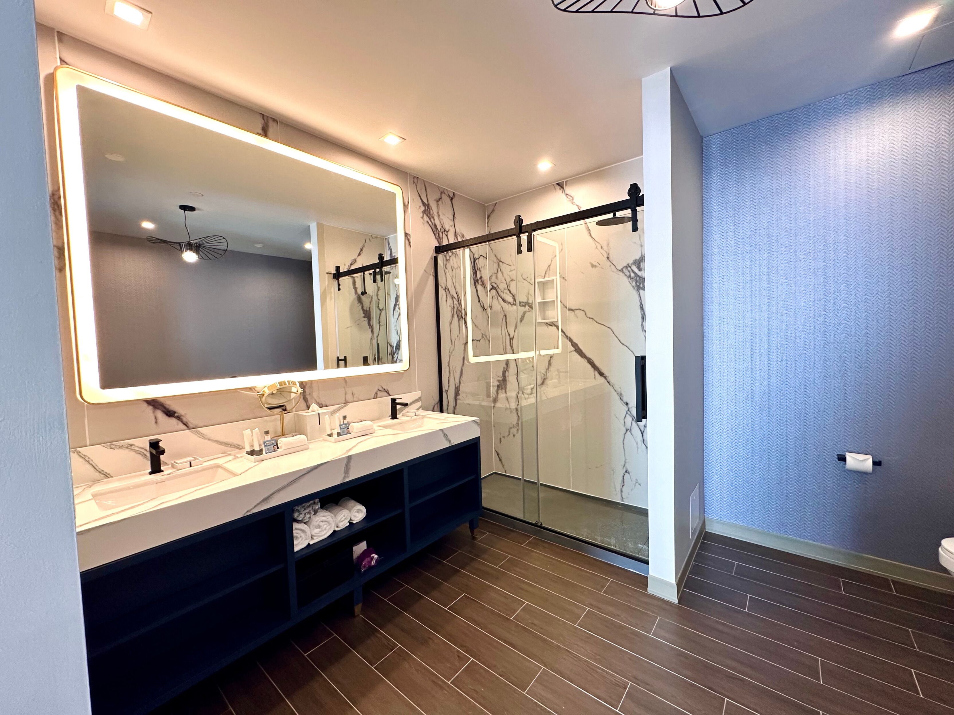 Une salle de bain moderne dotée d’un grand miroir, de deux lavabos, d’un meuble-lavabo et d’un espace douche.