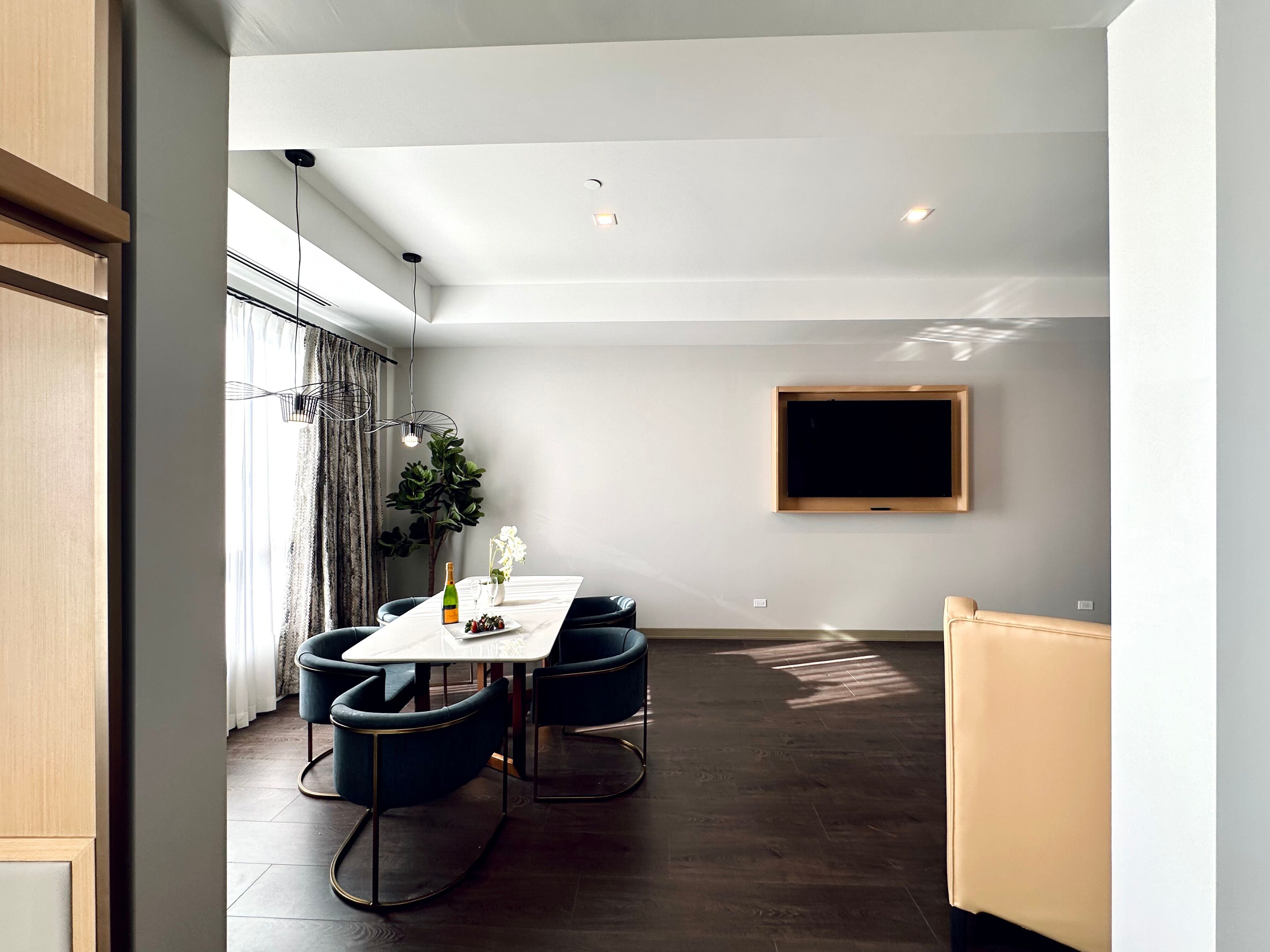 Un comedor moderno con una mesa blanca, sillas oscuras y un amplio ventanal con cortinas.