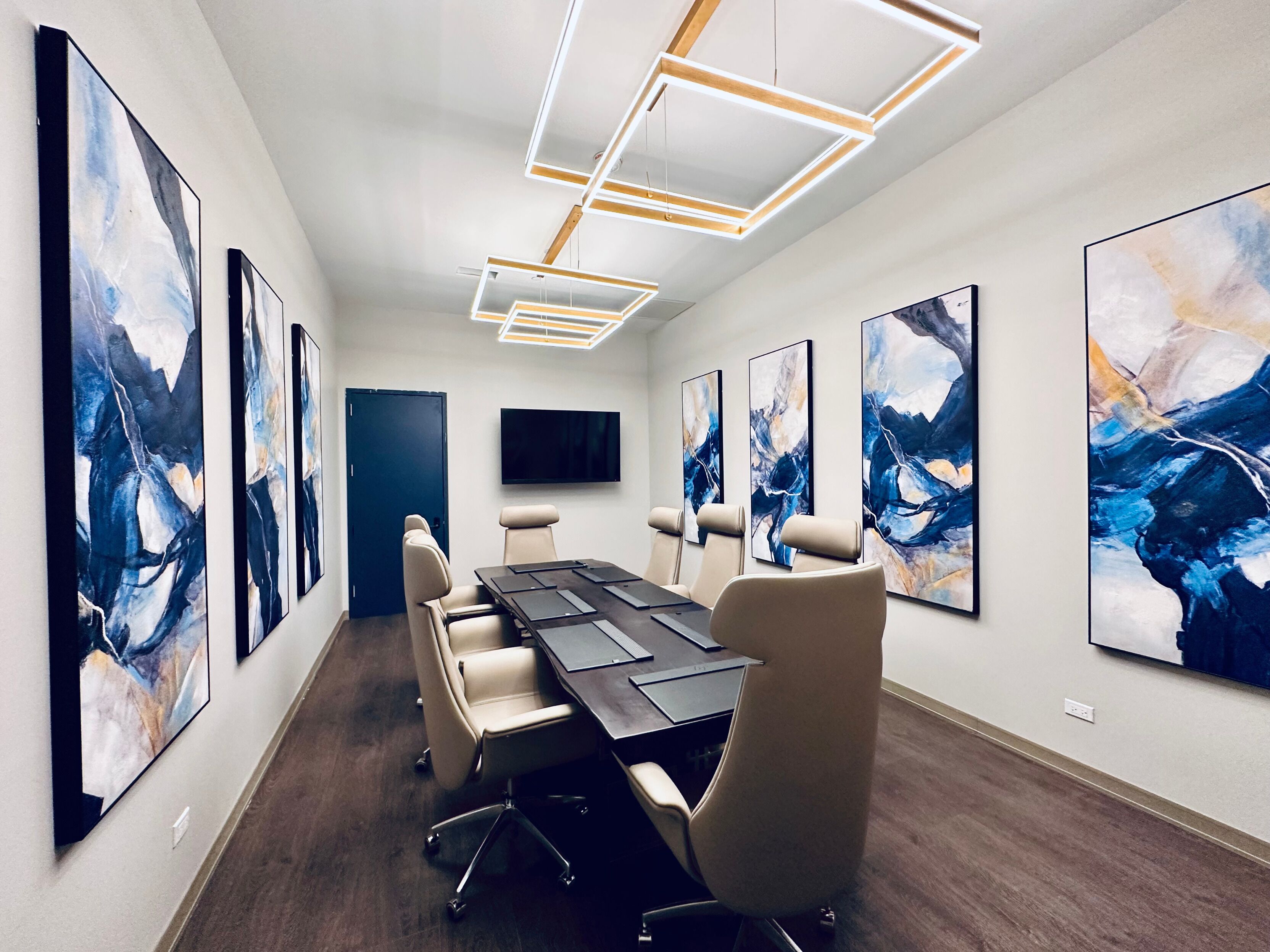 A conference room with a long table, six chairs, and abstract art on the walls.