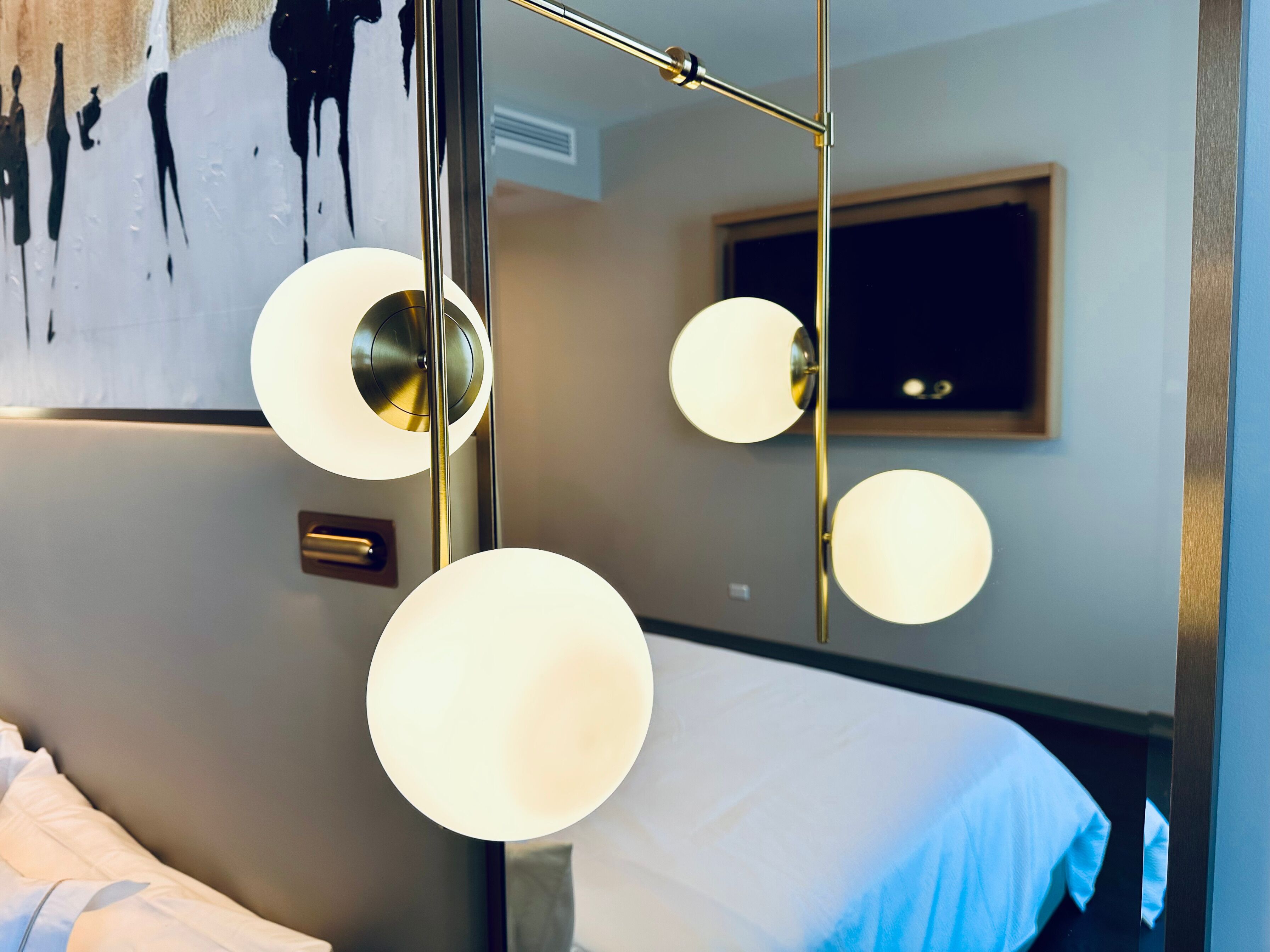 Una habitación de hotel moderna con una cama grande, un espejo con iluminación integrada y un diseño de pared minimalista.