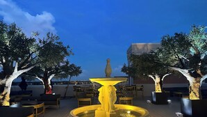 A rooftop terrace with a central fountain, seating areas, and trees. - Chez Hotel Arlington Heights (Arlington Heights)