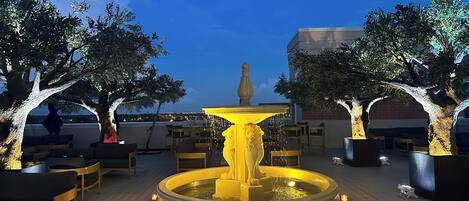 A rooftop terrace with a central fountain, seating areas, and trees.