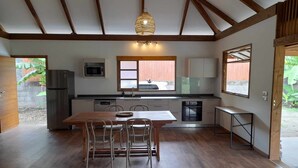 A compact kitchen with a dining area, wooden beams, a hanging light fixture, and a view of the outside. - Fare Pitate (Paea)