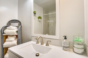 A bathroom with a white sink, a mirror, a wicker chair with towels, a bottle of hand soap, and a glass jar with cotton swabs. - 2BR Near Old Town & MGM First-Level Unit (Alexandria)