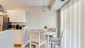 Cocina compacta con armarios blancos, un microondas y una lámpara colgante.