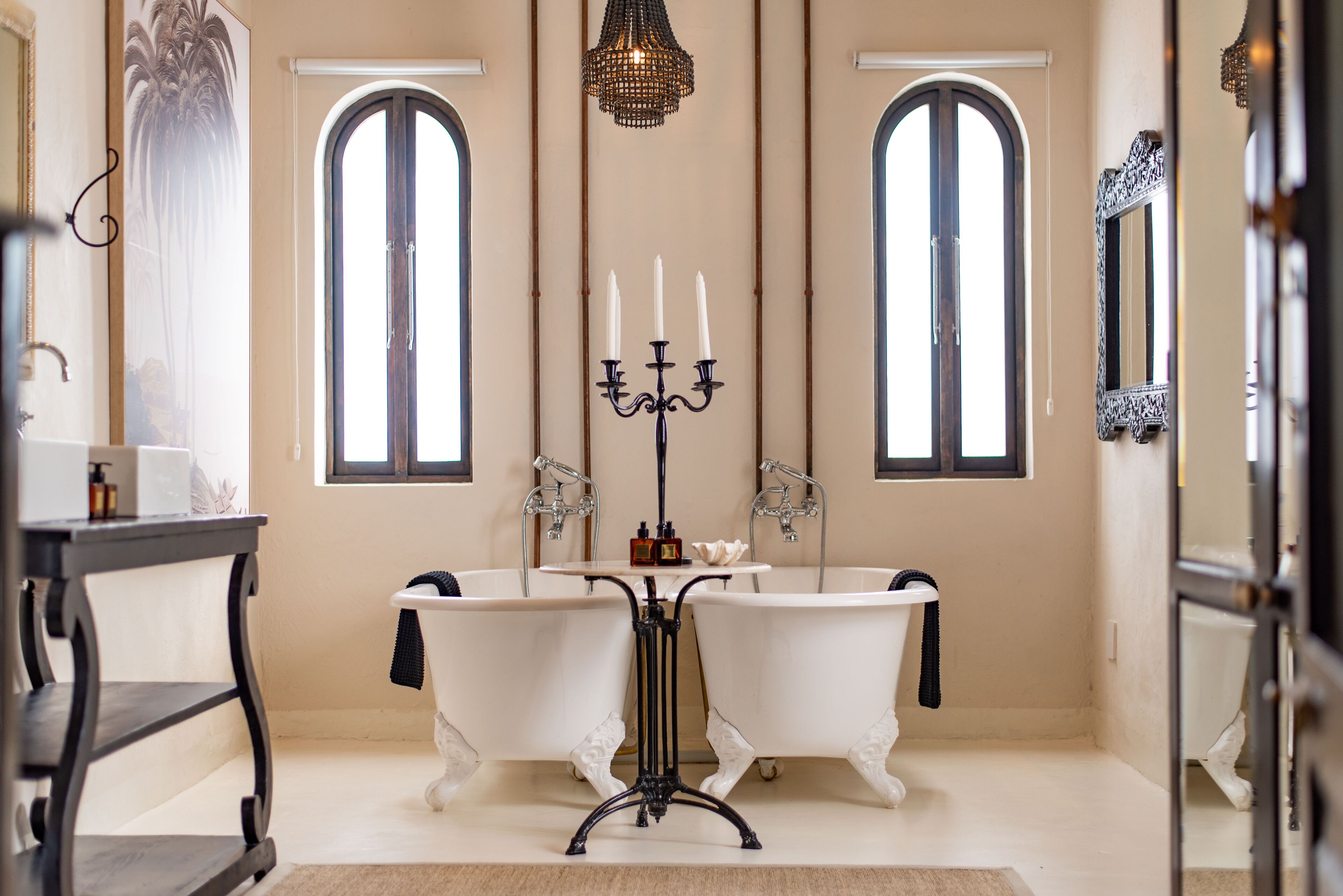 A bathroom with two clawfoot tubs, a chandelier, and a mirror.