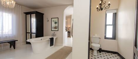 Een ruime badkamer met een vrijstaand bad, een toilet en een wastafelmeubel.