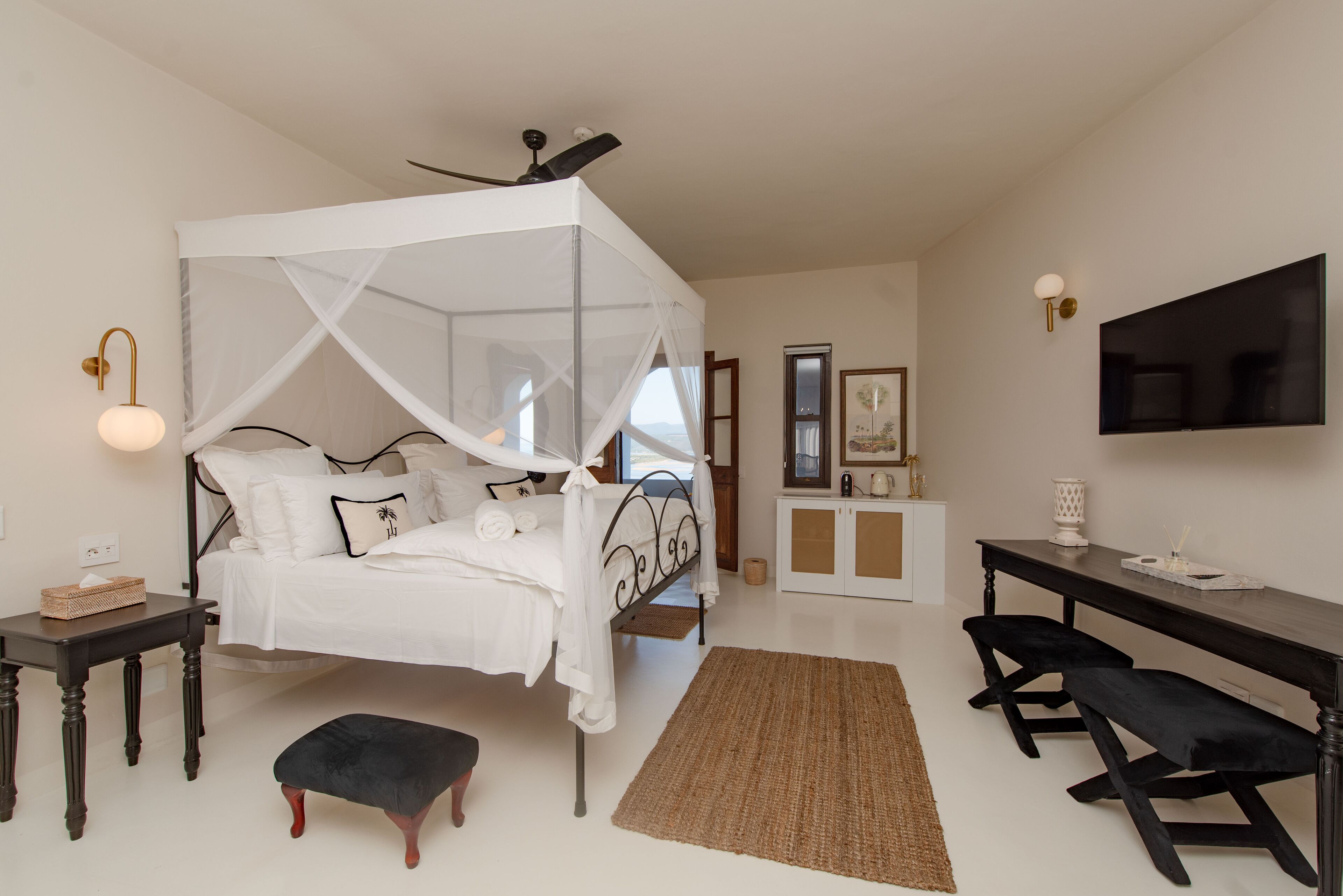 Un dormitorio con cama con dosel, un escritorio, un banco y un televisor en la pared.