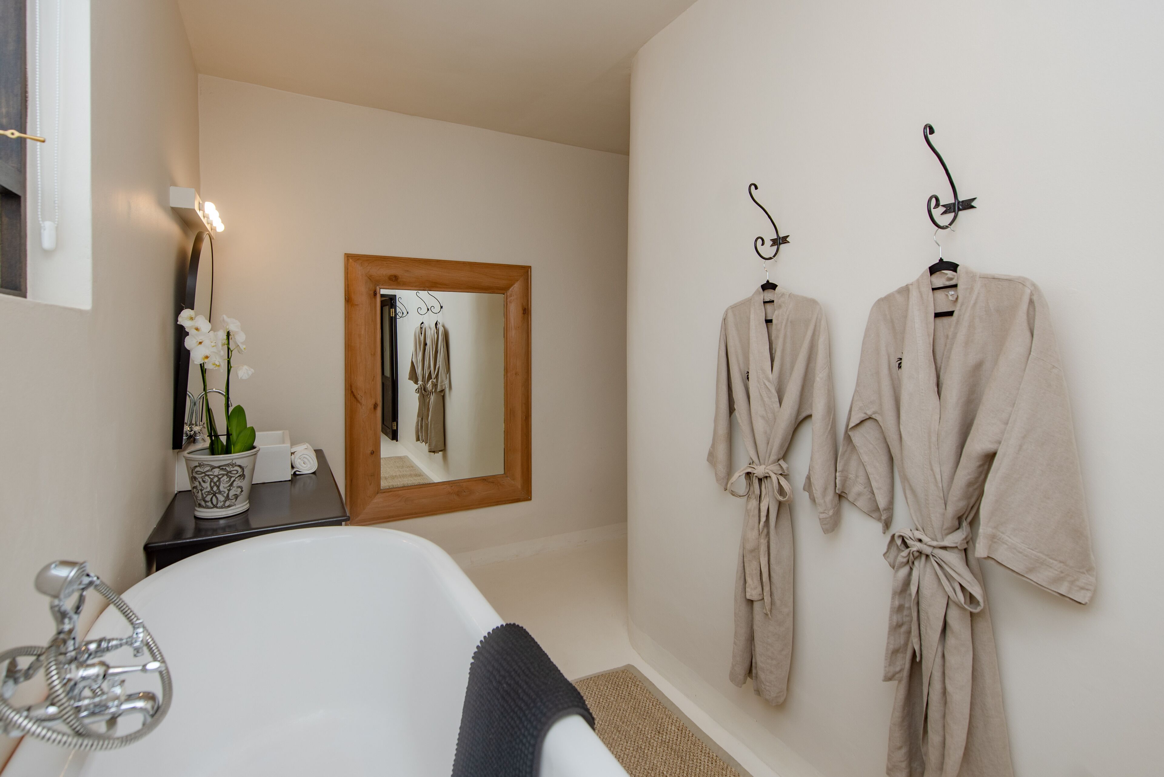 A bathroom with a bathtub, a mirror, and two robes hanging on hooks.