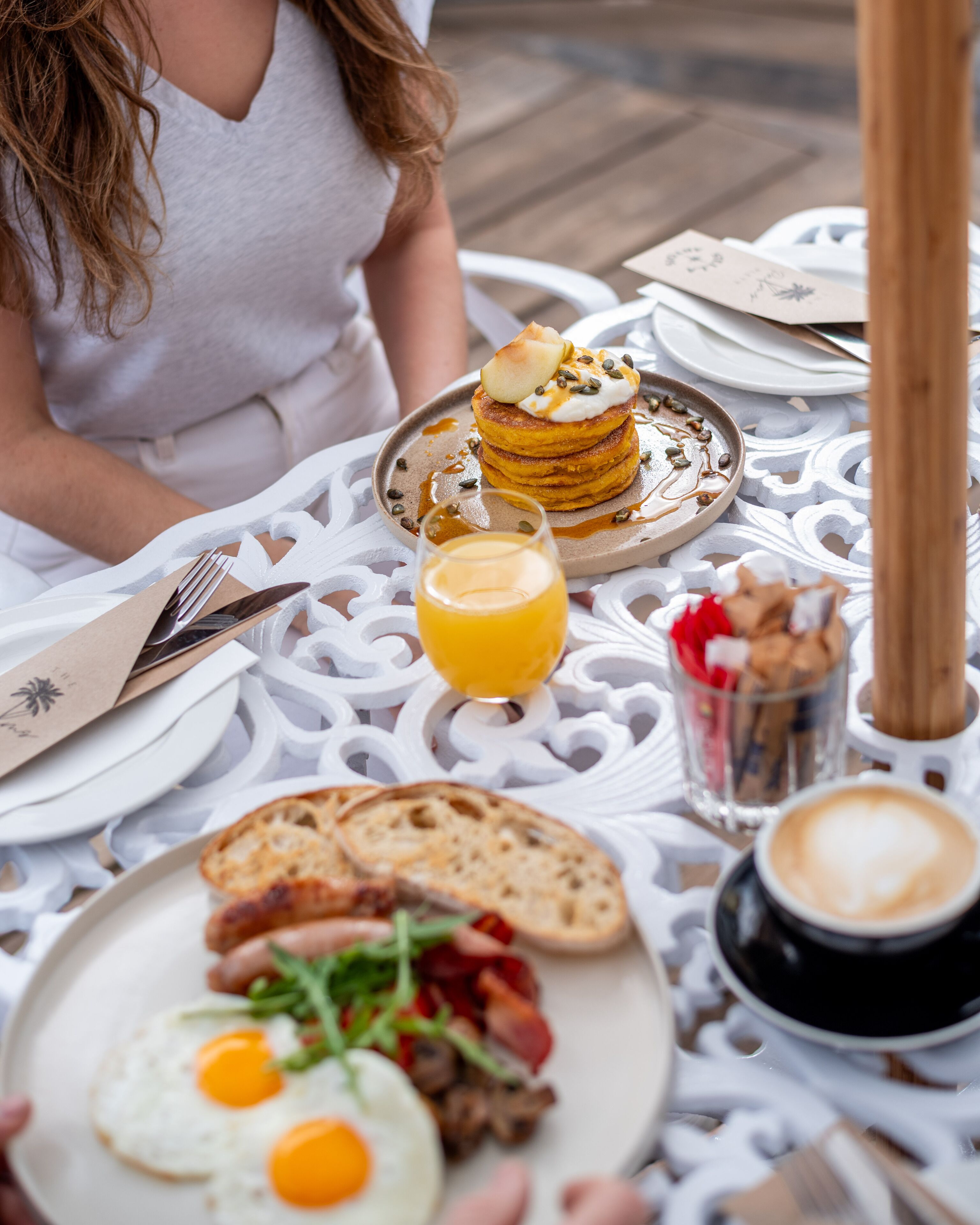 A breakfast setting with pancakes, eggs, toast, and coffee on a white table.