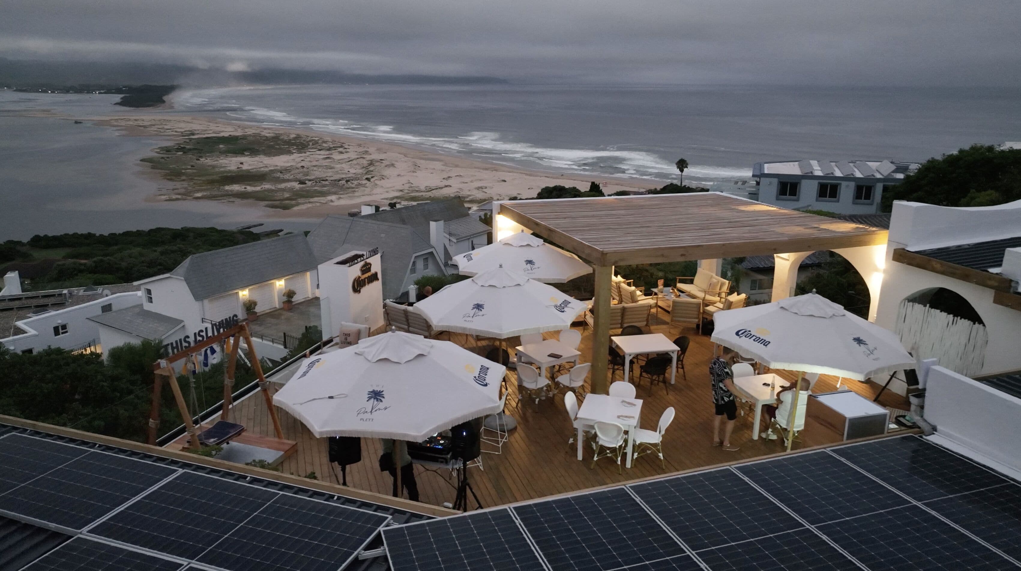A rooftop patio with solar panels, outdoor seating, and a view of the beach and ocean.