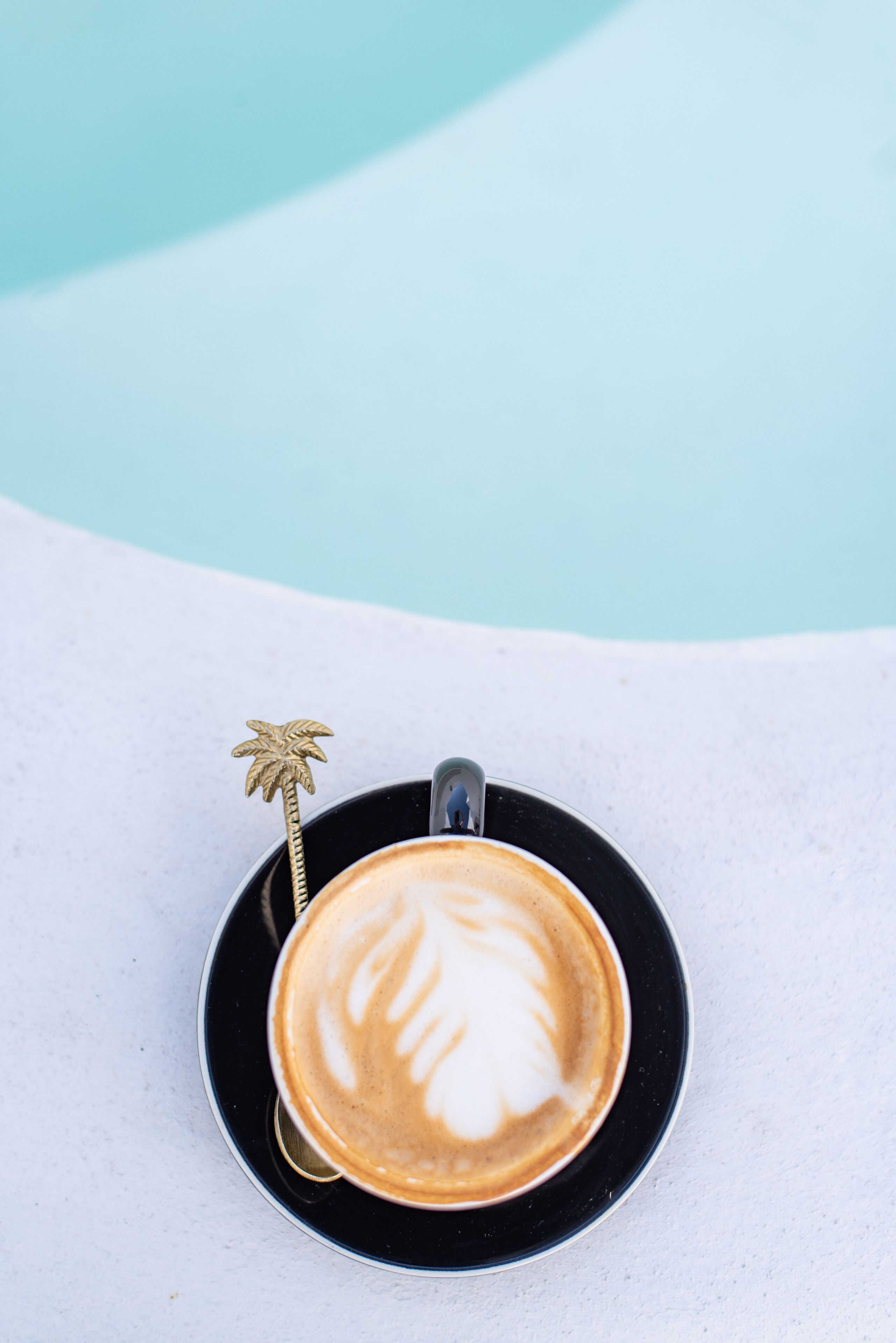 A cup of coffee with latte art on a black saucer, placed on a white surface.