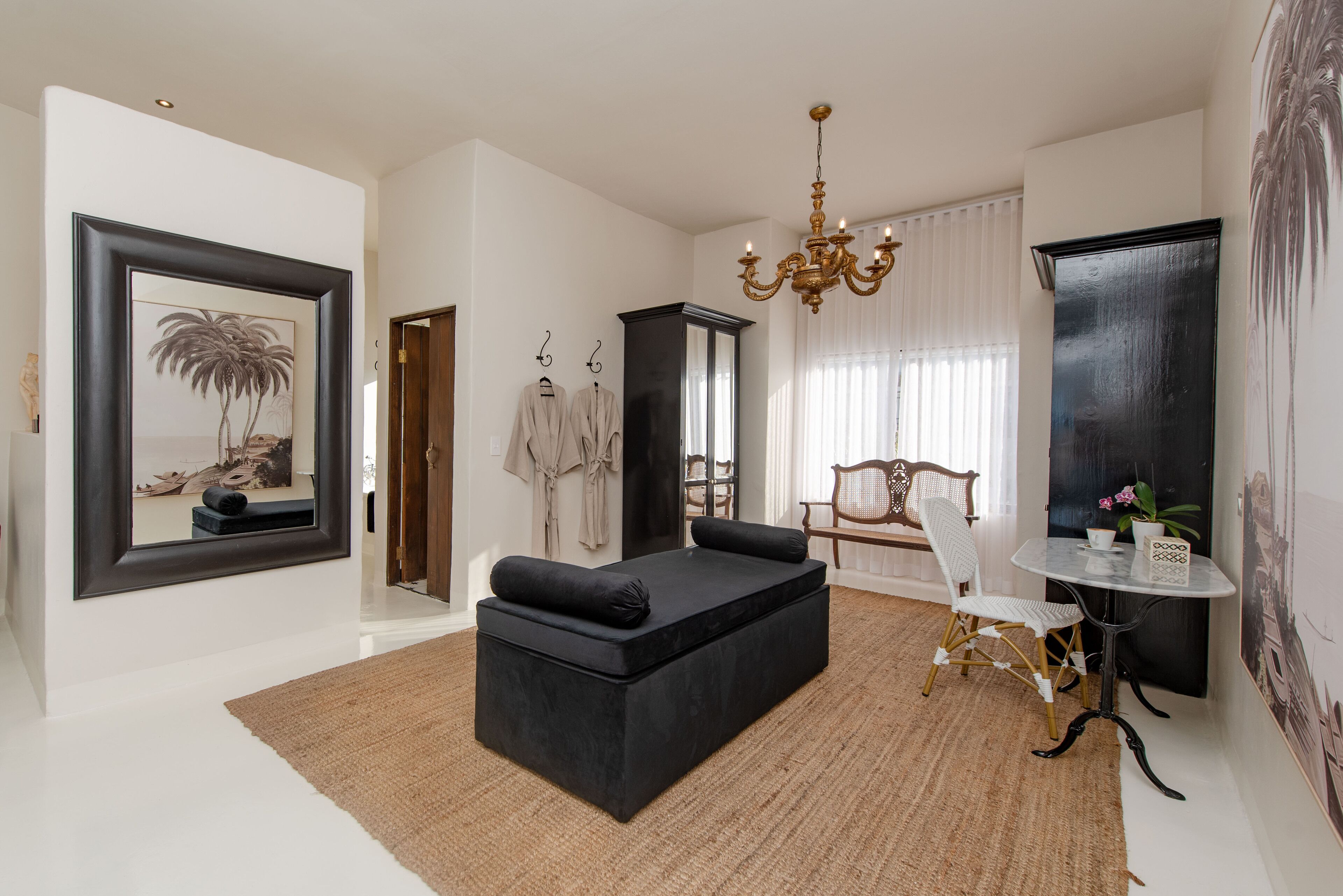 A modern living room with a black sofa, a dining table, and a chandelier.