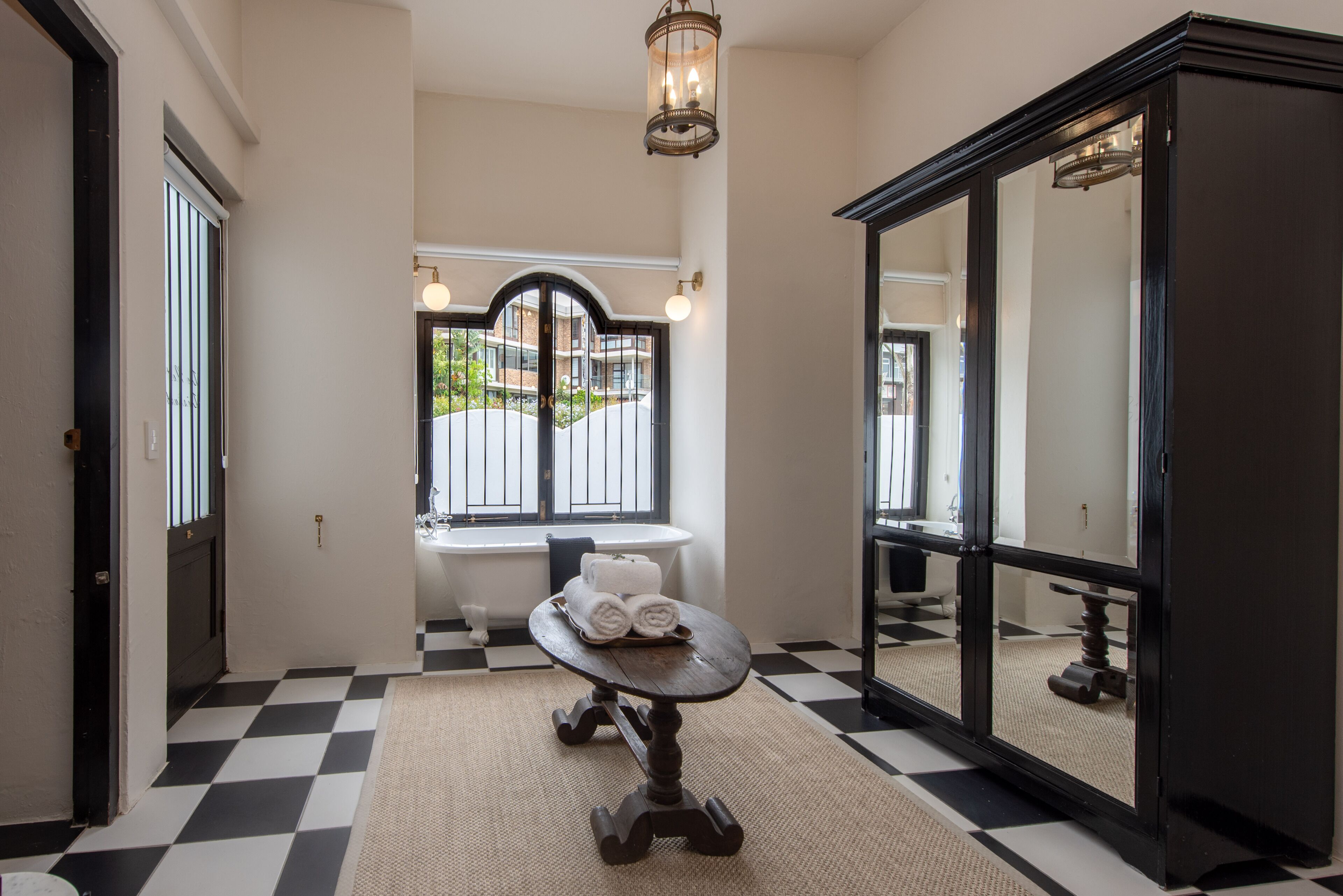 A bathroom with a checkered floor, a round table with towels, a bathtub, and a large mirror.