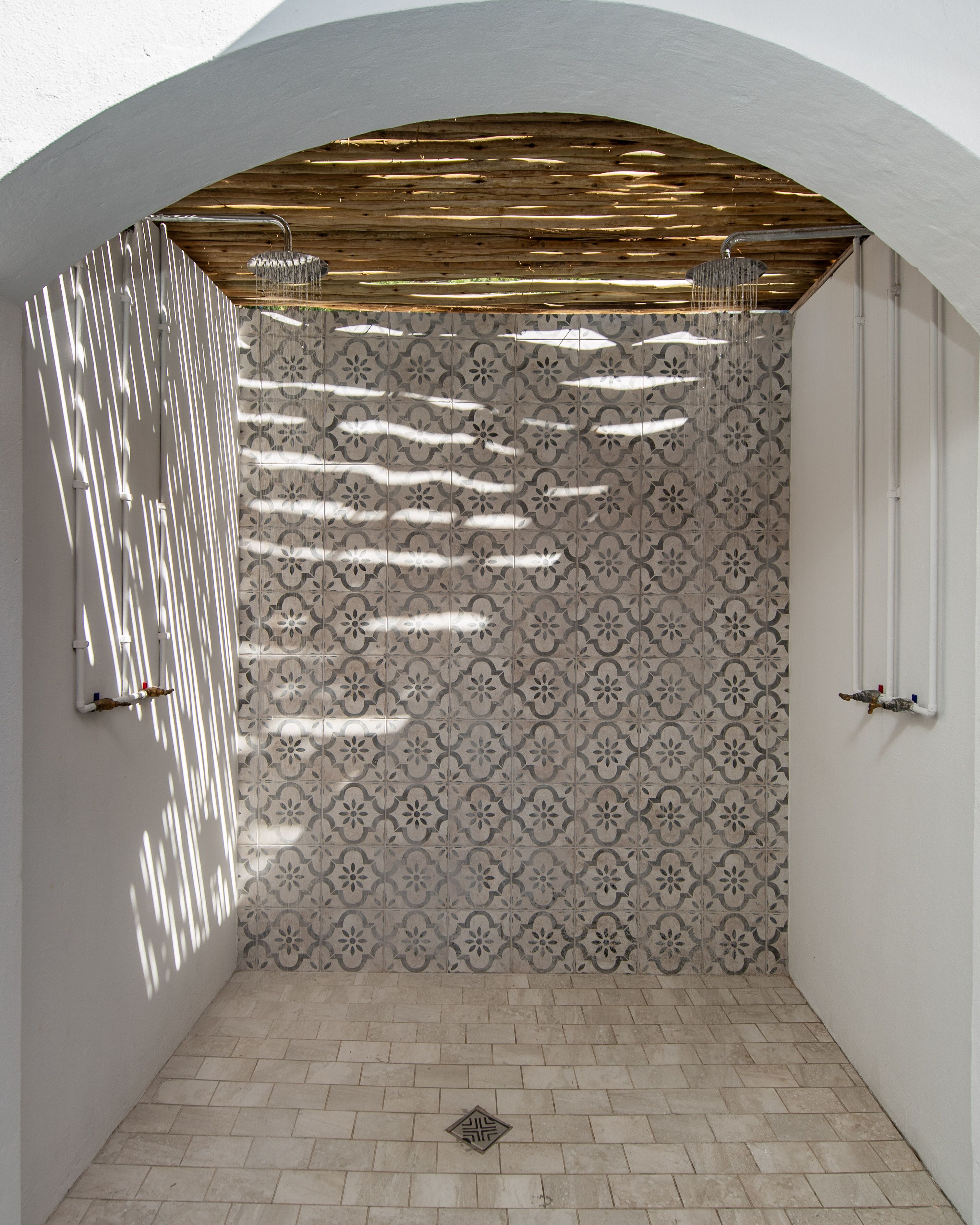 A shower area with a patterned tile wall, a wooden ceiling, and a tiled floor.