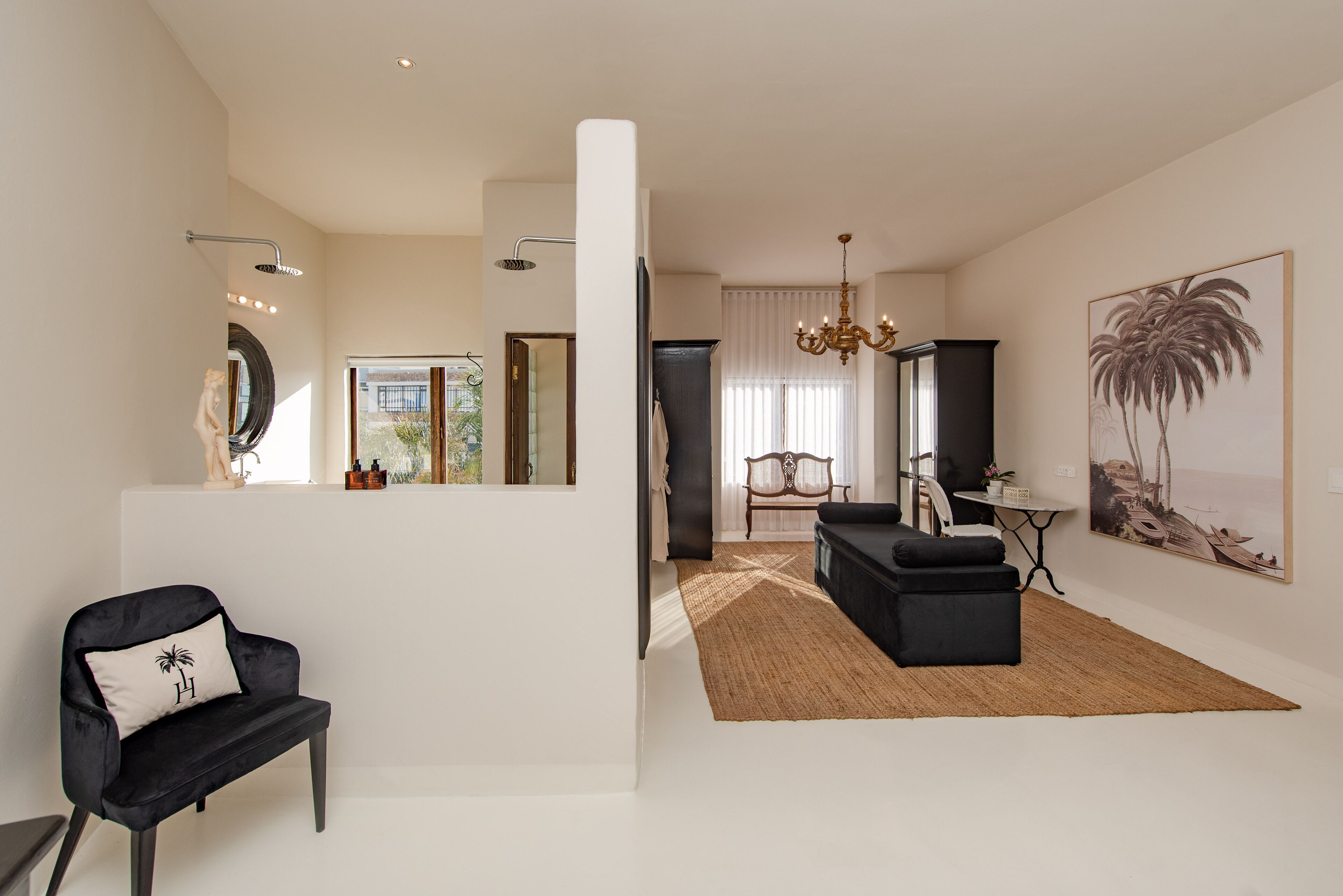 A modern living room with a black sofa, a black armchair, a woven rug, and a large painting of a palm tree.