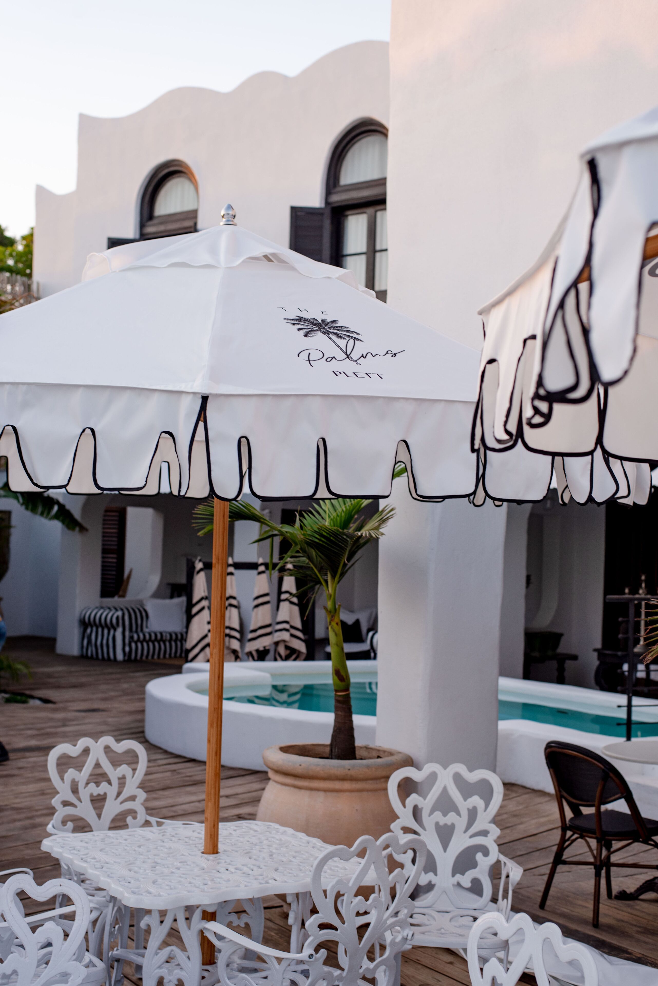 A patio area with white outdoor furniture, a white umbrella, and a pool.