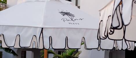 A patio area with white outdoor furniture, a white umbrella, and a pool.