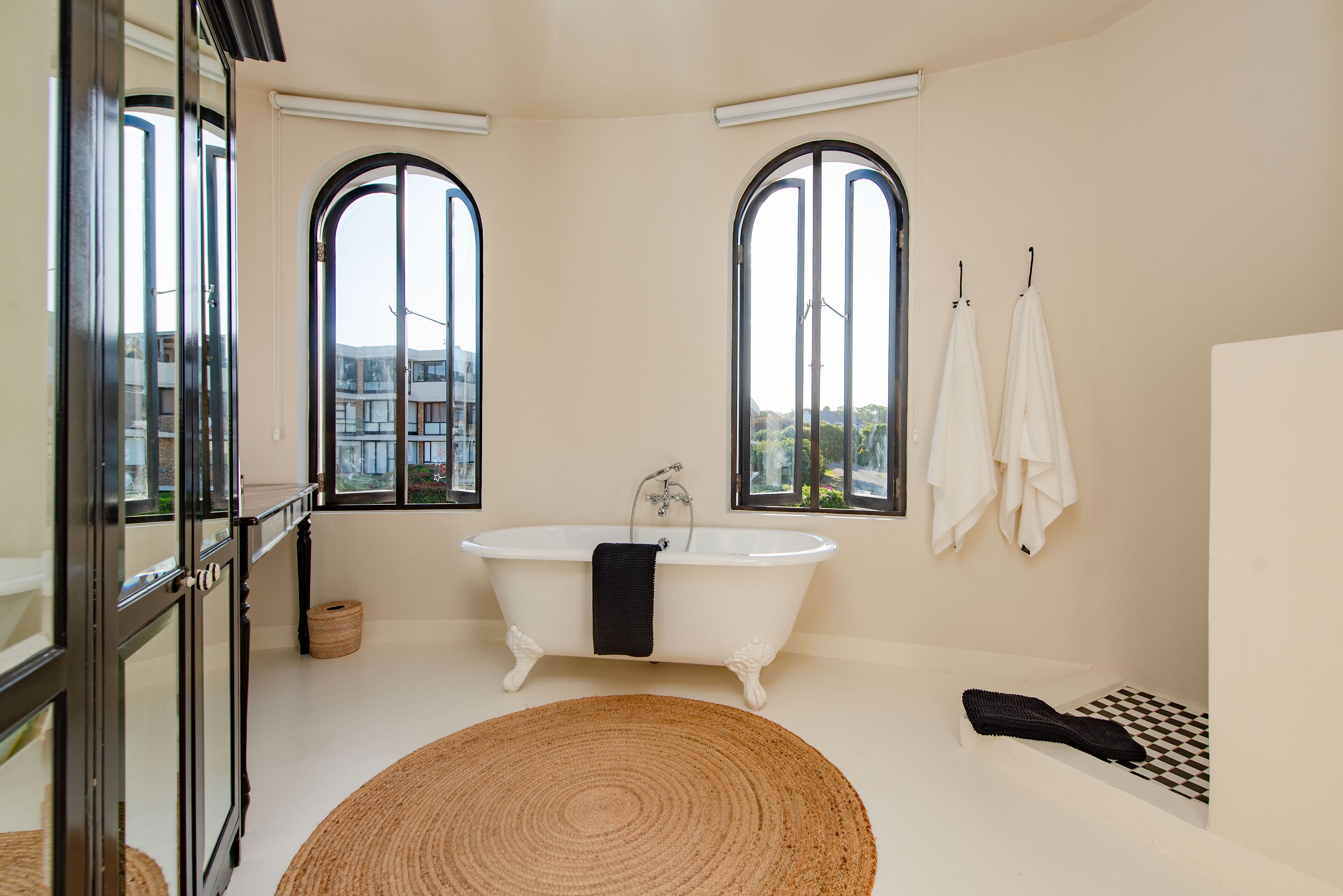 A bathroom with a freestanding bathtub, large arched windows, and a checkered floor.