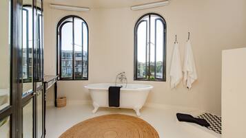 A bathroom with a freestanding bathtub, large arched windows, and a checkered floor.