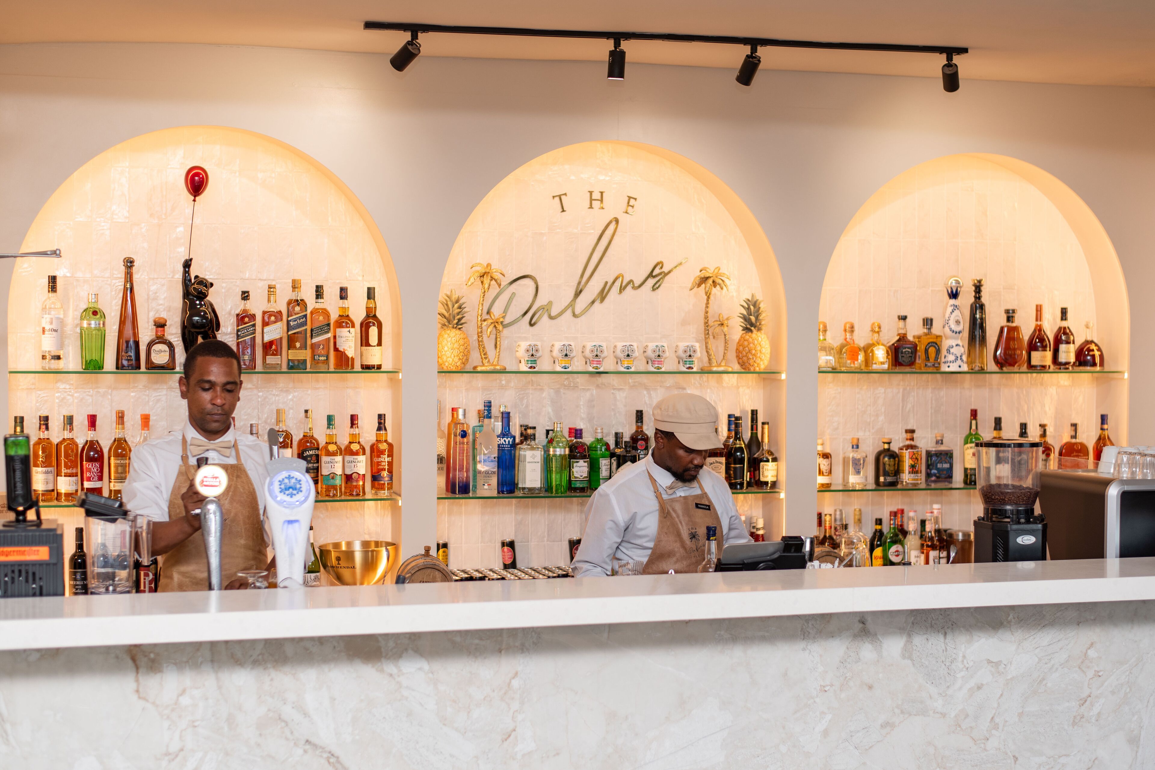 A bar with two bartenders, shelves of liquor bottles, and a sign reading "THE Palms."