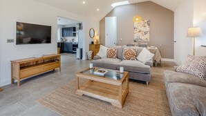 A modern living room with a sofa, coffee table, and TV. A kitchen is visible in the background. - 2 bedroom accommodation in Trefor Nr Caernarfon (Trefor Nr Caernarfon)