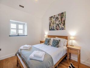 Ein Schlafzimmer mit einem Bett, zwei Nachttischen, einem Fenster und einem an der Wand hängenden abstrakten Gemälde.