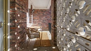 Un couloir étroit aux murs de briques, avec un plafond blanc et un mur orné sur le côté droit. Au centre, on trouve une table entourée de chaises et un tapis.