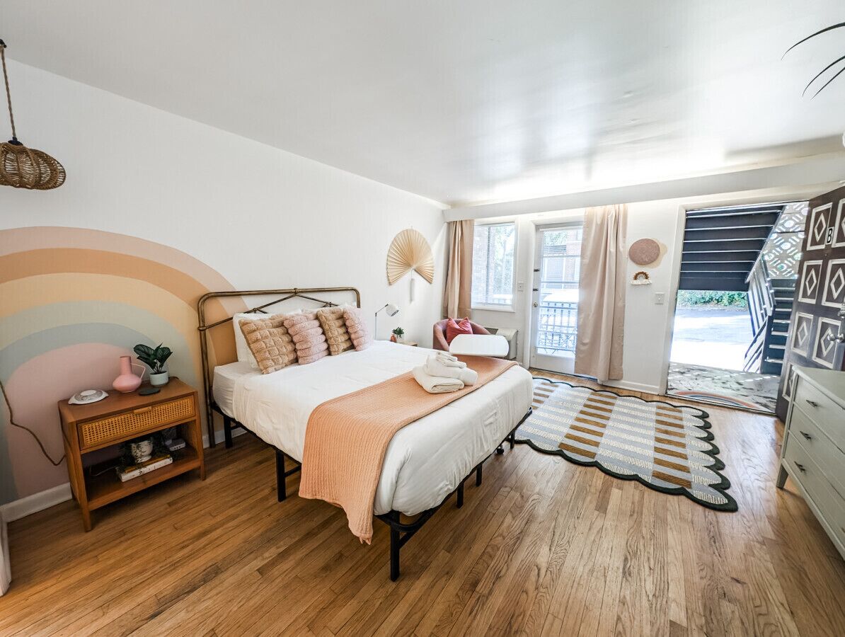 A bedroom with a bed, bedside table, lamp, and a view of the outdoors.