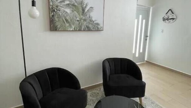 Un salon moderne avec deux fauteuils noirs, une petite table noire ornée d’une plante, un lampadaire et un tableau encadré accroché au mur.