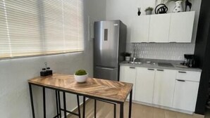 Une cuisine de taille réduite avec une table en bois, un réfrigérateur et des placards blancs.
