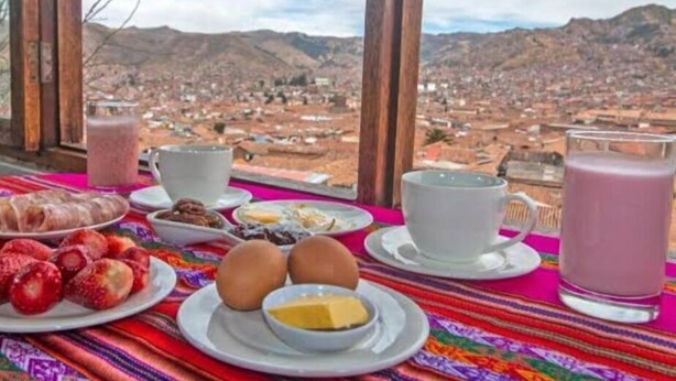 A breakfast table with various foods and drinks, set against a backdrop of a mountainous landscape. - Black Sheep Cusco (Cusco)