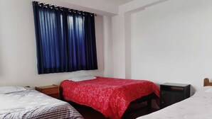 A bedroom with two single beds, a red bedspread, a nightstand, a dresser, and a window with blue curtains. - Black Sheep Cusco (Cusco)
