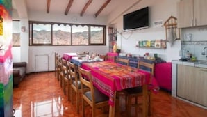A dining area with a long table, chairs, and a view of the mountains through large windows. - Black Sheep Cusco (Cusco)