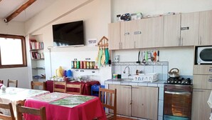 A kitchen with wooden cabinets, a gas stove, a microwave, and a dining area with a table covered in a red tablecloth. - Black Sheep Cusco (Cusco)